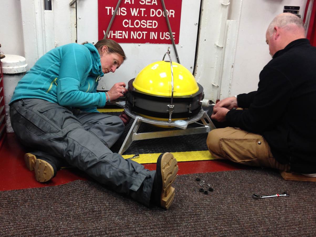 WHOI technicians Dara Tebo and Tim Kane attach a heavy tripod  to a seismometer pressure housing prior to BBOBS deployment.  The tripod helps couple the seismometer to ground motion.
