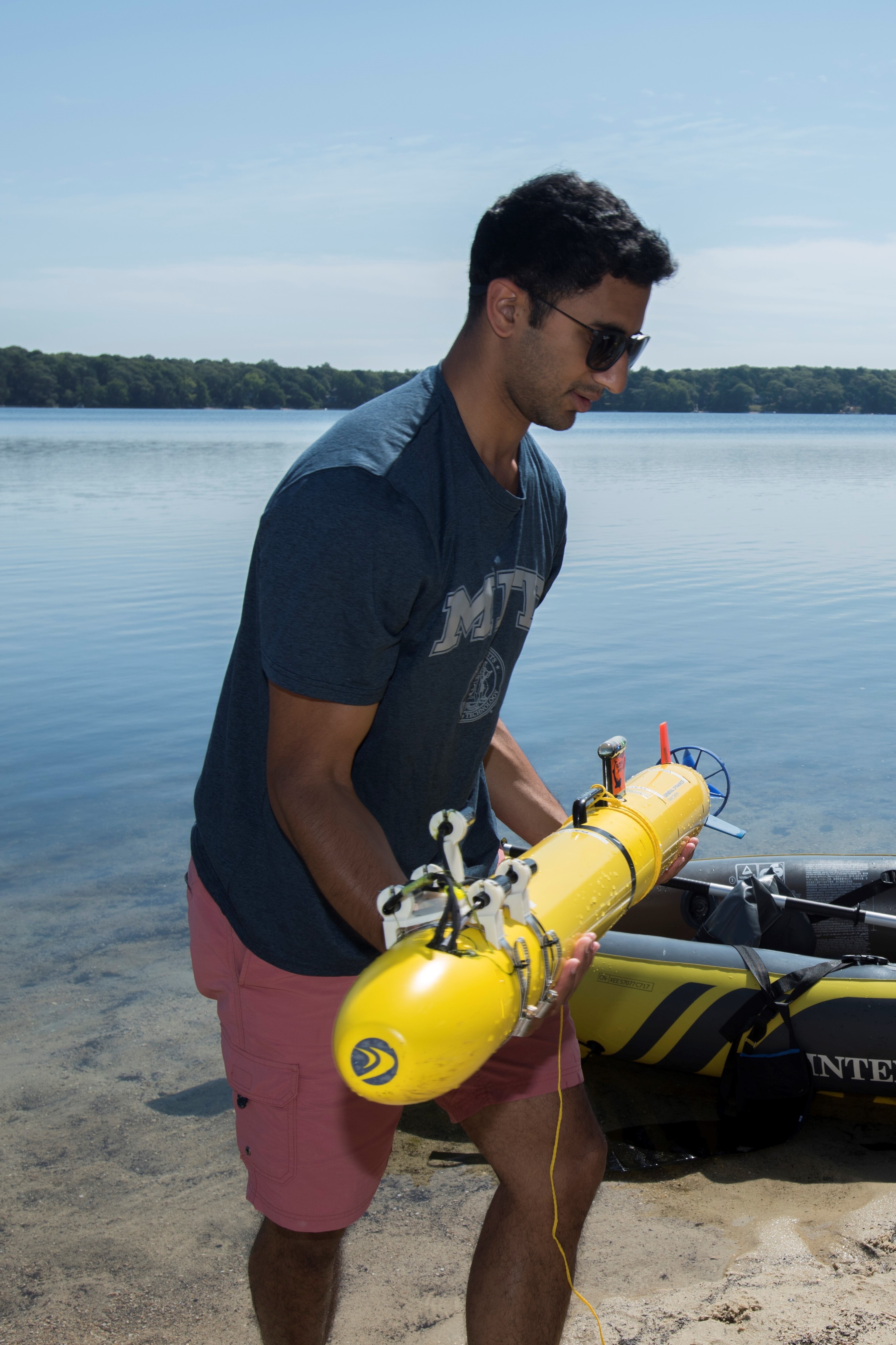EeShan Bhatt cradles an autonomous underwater vehicle (AUV) in between test trials at Ashumet Pond, Falmouth, MA.
