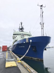Photo of large ship with blue hull tied up at the dock. The Icelandic national flag is flying from the ship.