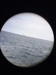 Photo of a ship at sea, the US vessel R/V Armstrong. The image is surrounded with a black circle because the camera had to focus through an eye of a pair of binoculars.